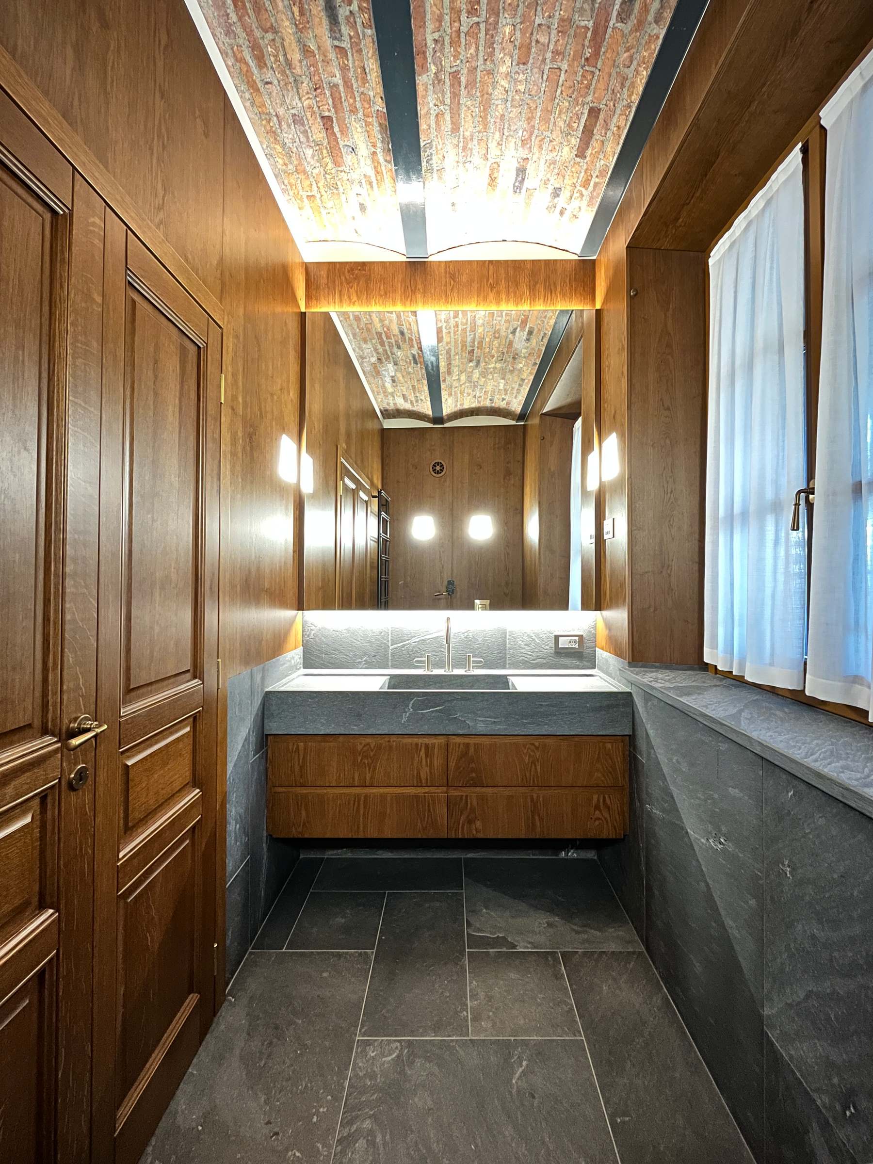 Continuità sartoriale: le sale da bagno su misura coordinate alle porte in massello della residenza. — 
